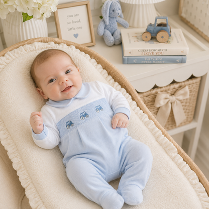 Baby in a blue outfit with tractor patterns lying in a crib with a decorative background.