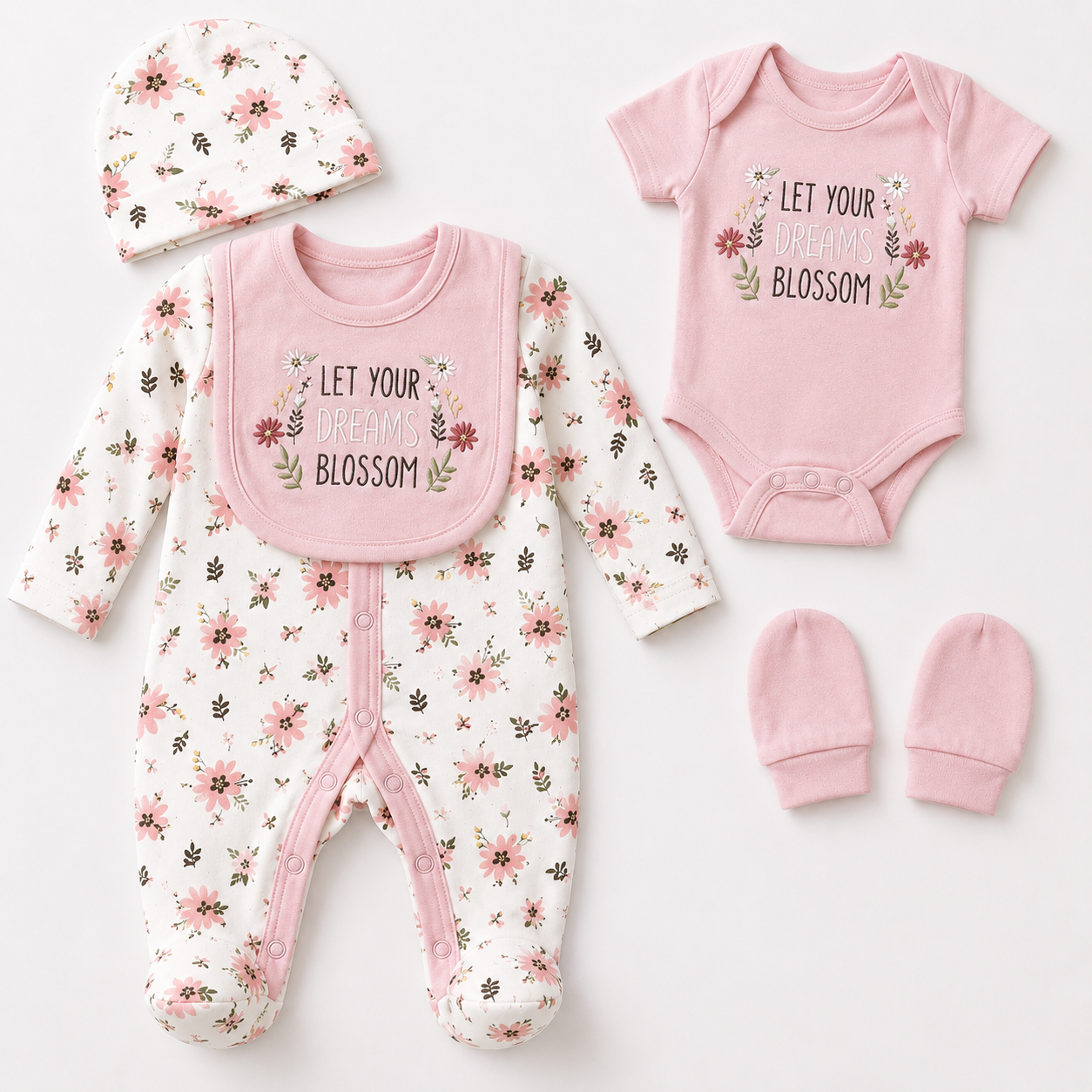 A coordinated baby clothing set laid flat on a white background, including a floral one-piece outfit with a pink bib, a pink bodysuit printed with the words 'LET YOUR BLOSSOM BLOSSOM,' a matching floral hat, and a pair of pink mittens.