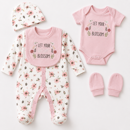 A coordinated baby clothing set laid flat on a white background, including a floral one-piece outfit with a pink bib, a pink bodysuit printed with the words 'LET YOUR BLOSSOM BLOSSOM,' a matching floral hat, and a pair of pink mittens.