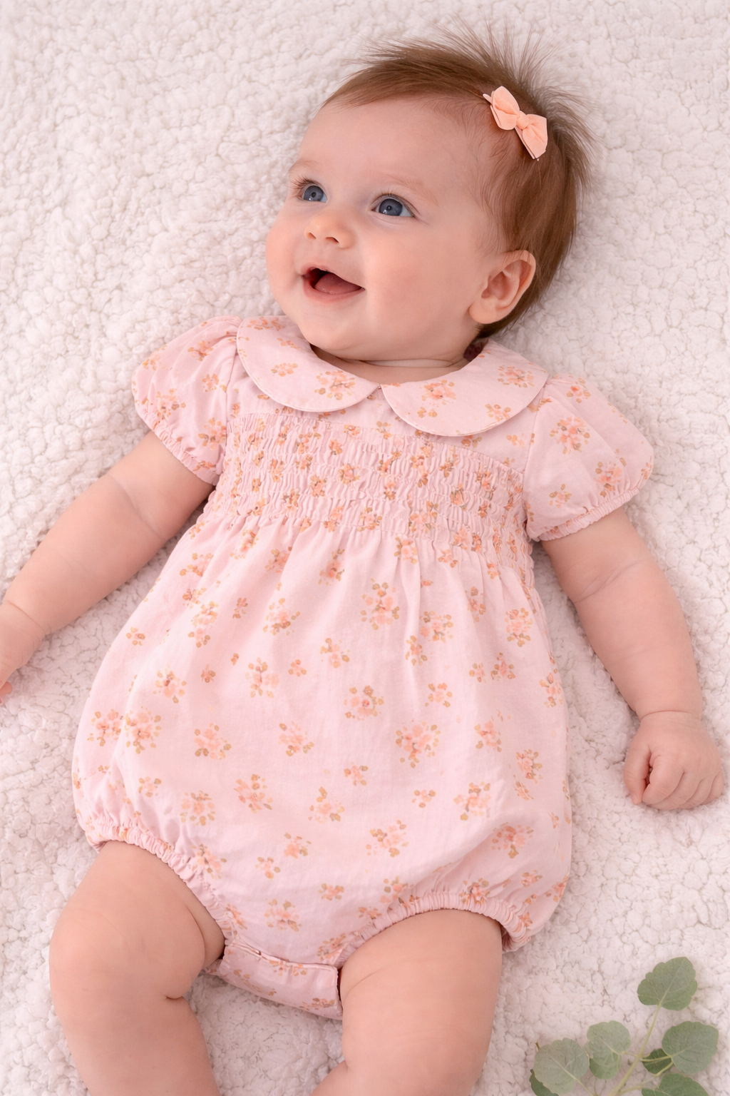 Baby girl wearing blush pink floral smocked bubble romper with Peter Pan collar and puff sleeves