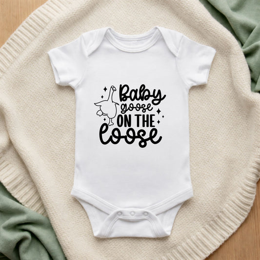White baby onesie with 'Baby goose on the loose' text on a textured surface