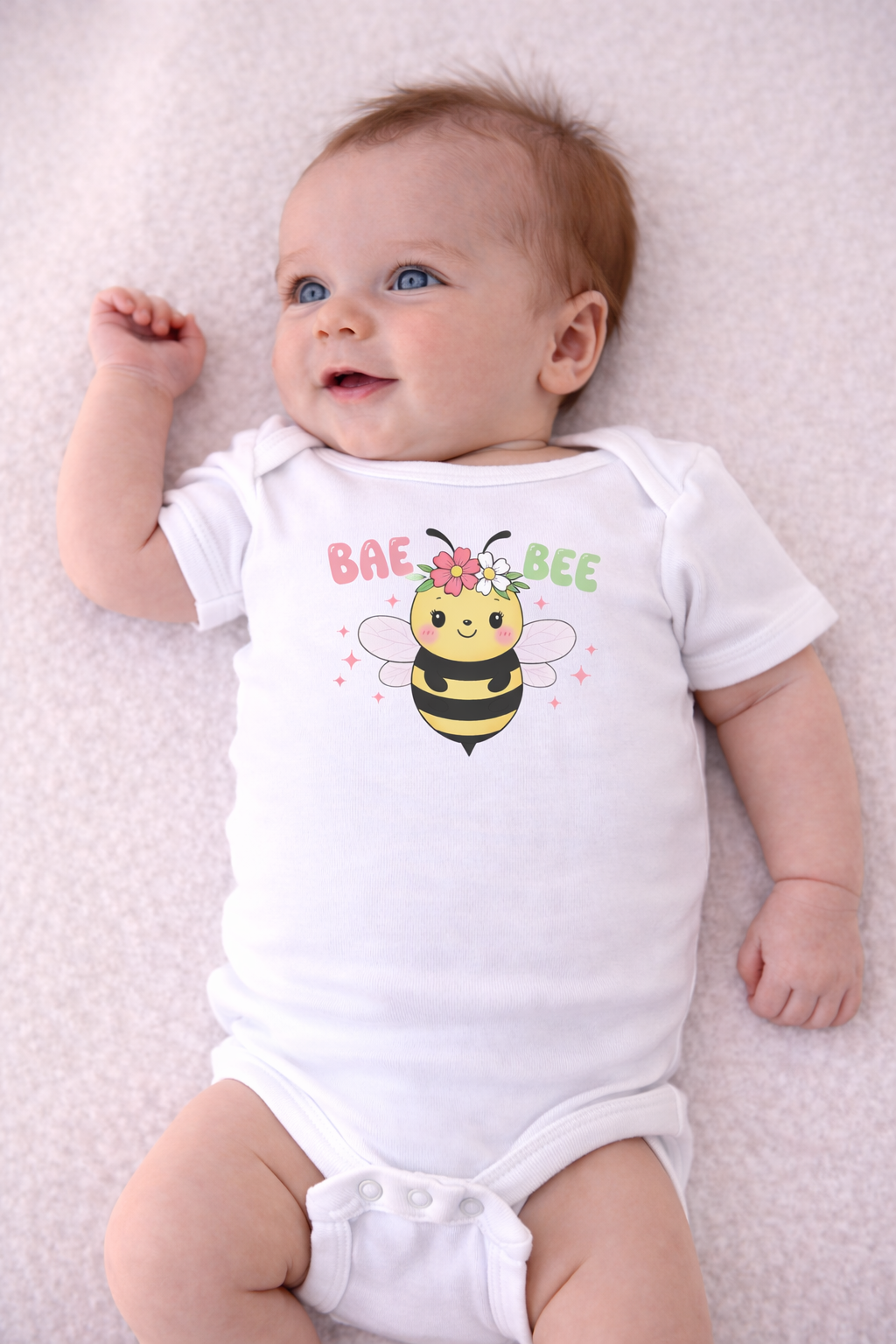 Baby wearing a white onesie with a bee design and text on a light pink background
