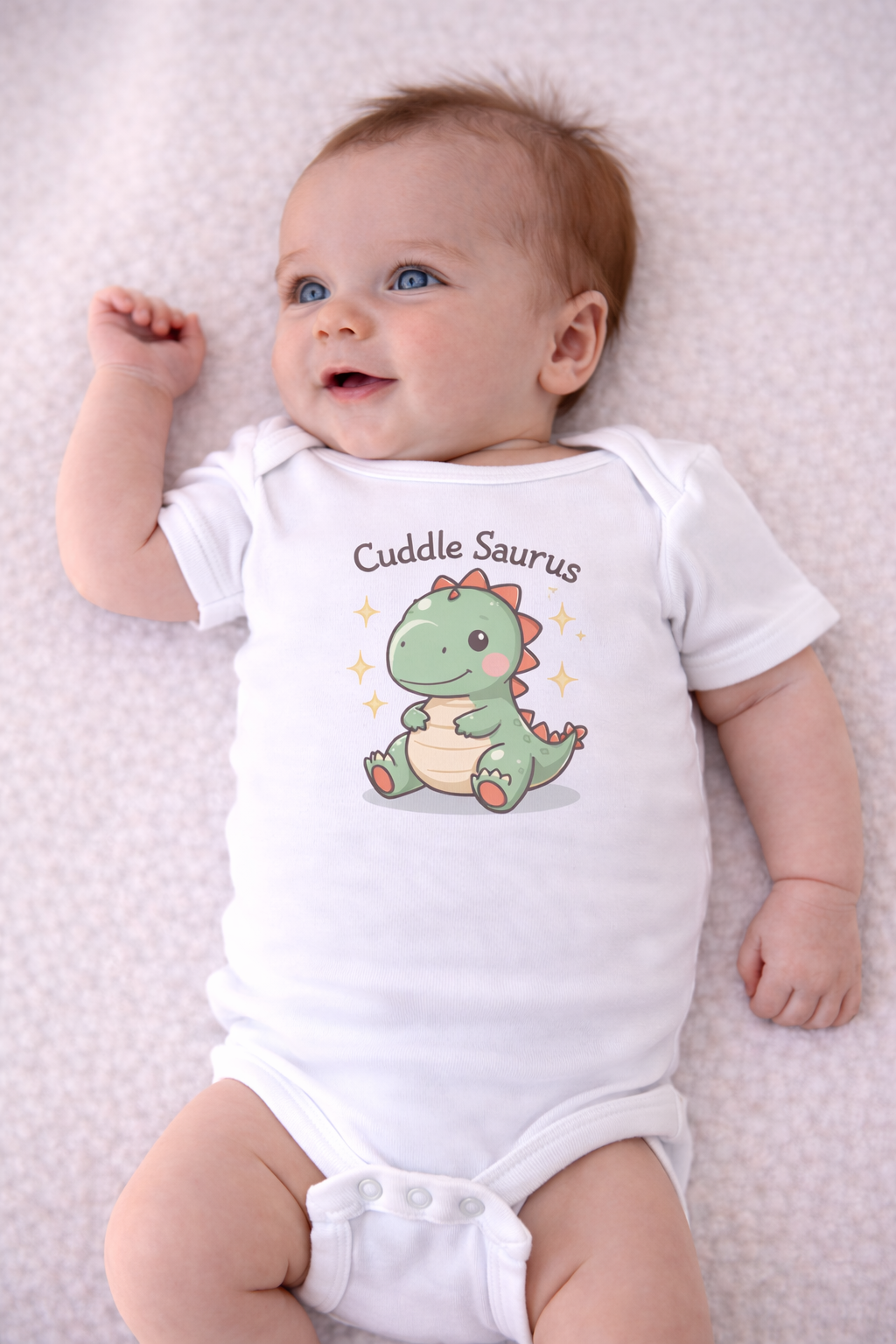 Baby wearing a white onesie with a dinosaur graphic and text on a light pink blanket