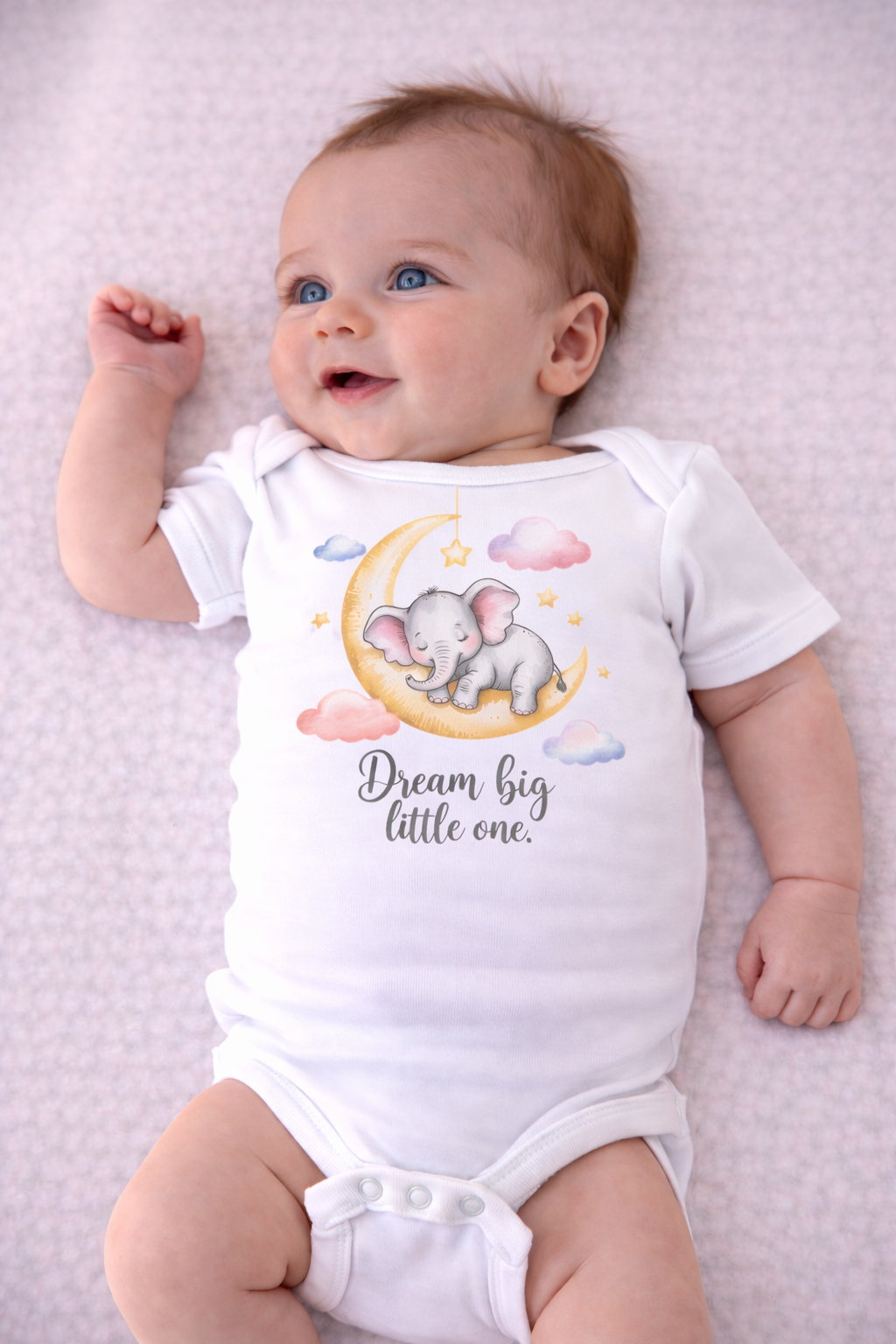 Baby wearing a onesie with an elephant design and text on a light purple blanket