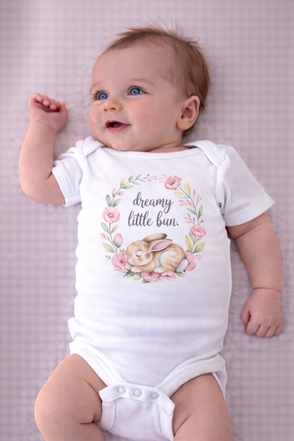 Baby wearing a white onesie with a bunny and floral design on a checkered background