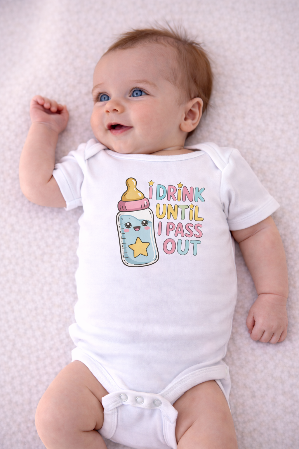 Baby wearing a white onesie with a colorful graphic and text on a light pink blanket.