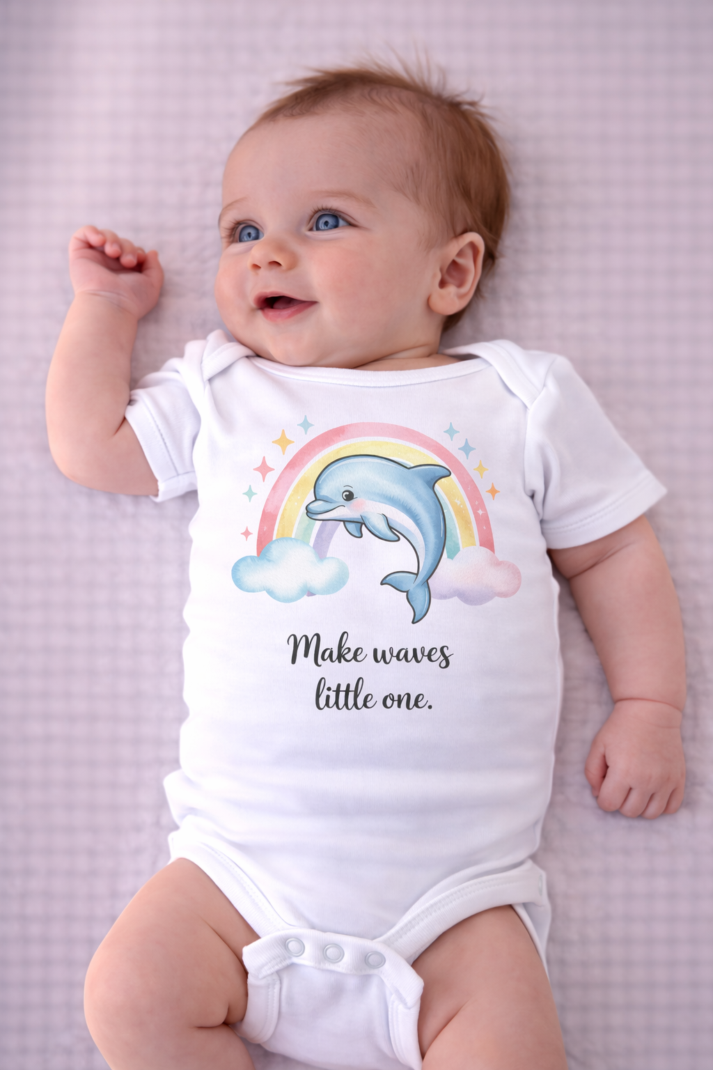Baby wearing a onesie with a dolphin and rainbow design on a pink checkered background