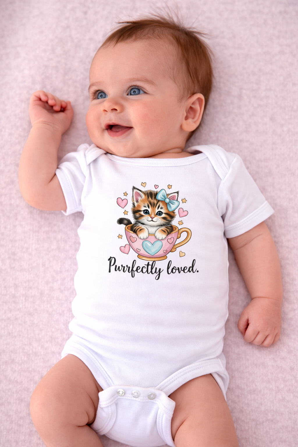 Baby wearing a white onesie with a cat design and 'Purrfectly loved' text on a pink background