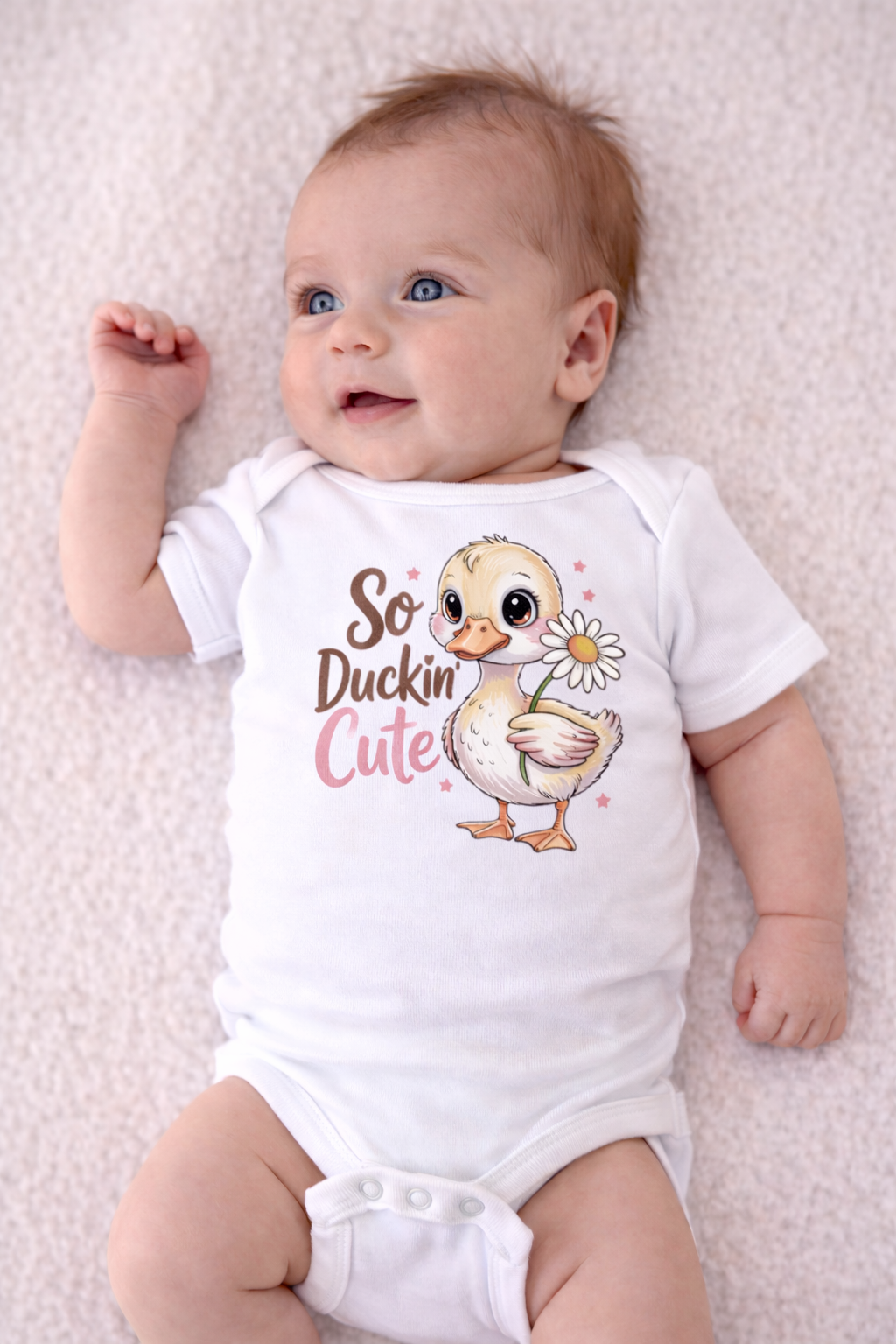 Baby wearing a white onesie with a duck graphic and text on a light pink background