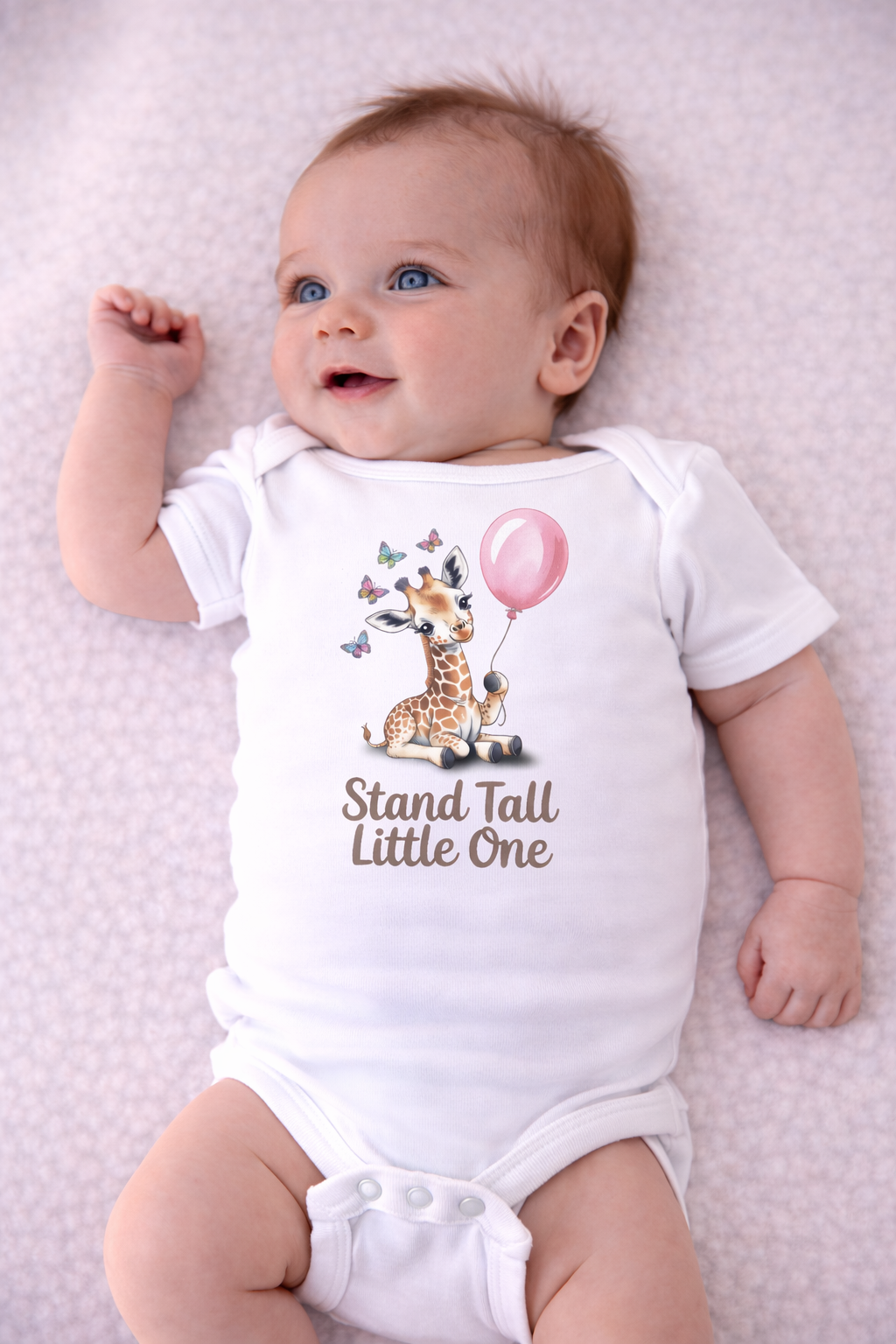 Baby wearing a onesie with a giraffe design and text on a light pink background