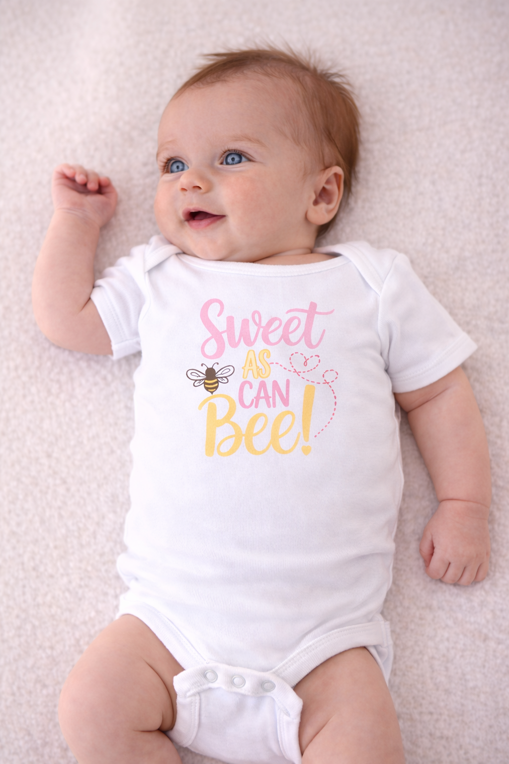 Baby wearing a white onesie with 'Sweet as can bee' text and graphics on a light background