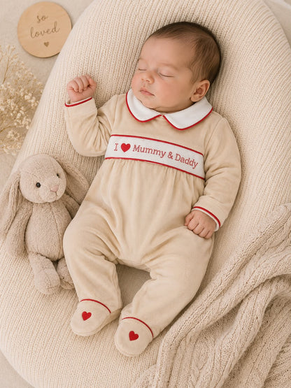 Baby wearing cream I Love Mummy and Daddy velour sleepsuit with red heart feet detail