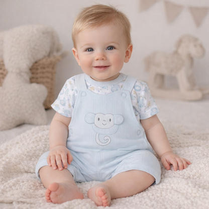 Baby wearing a light blue romper with a monkey design, sitting on a soft surface.