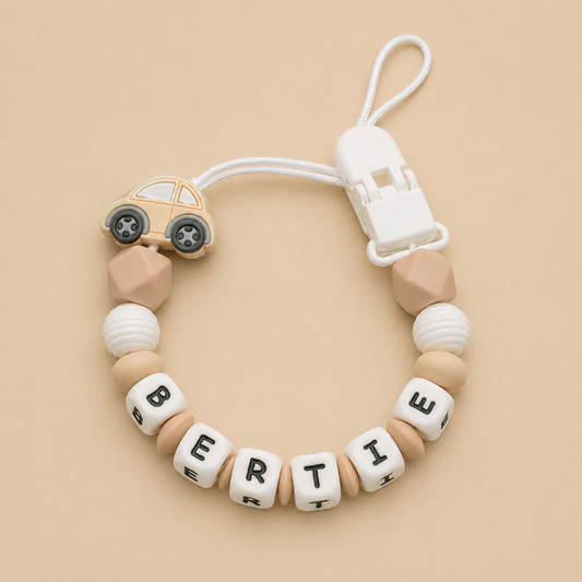 dummy clip with silicone car charm and letter beads spelling 'BERTIE' on a beige background
