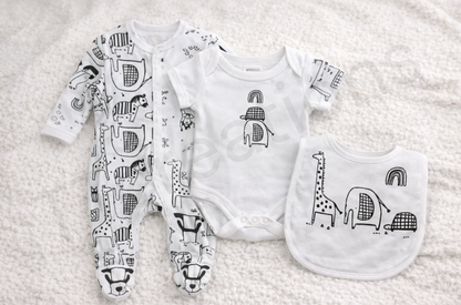 Monochrome safari-themed baby gift set featuring a patterned footed sleepsuit, short-sleeve bodysuit, and matching bib with giraffe, elephant, turtle and rainbow illustrations, laid flat on a soft cream background.