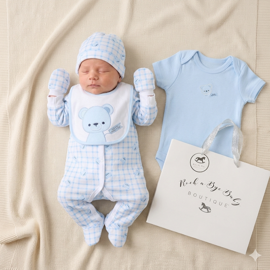 Newborn baby in blue checkered outfit with matching hat and baby onesie, next to a 'Rock a Bye Baby' bag on beige fabric.