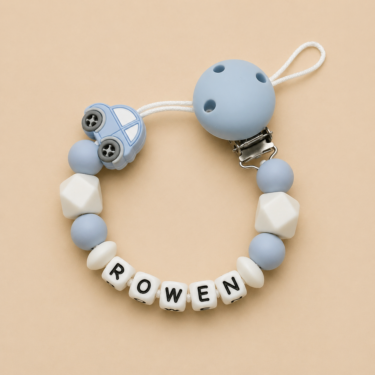Silicone dummy clip with car design and letter beads spelling 'ROWEN' on a beige background