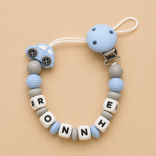 Baby dummy clip with blue car charm and letter beads spelling 'RONNIE' on a beige background
