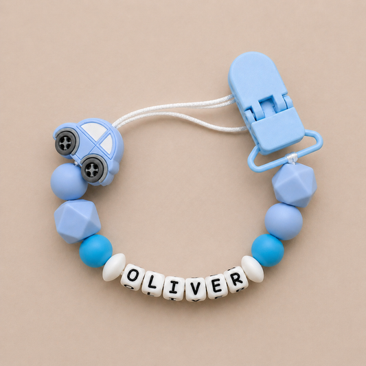 Blue baby dummy clip with 'OLIVER' beads on a beige background