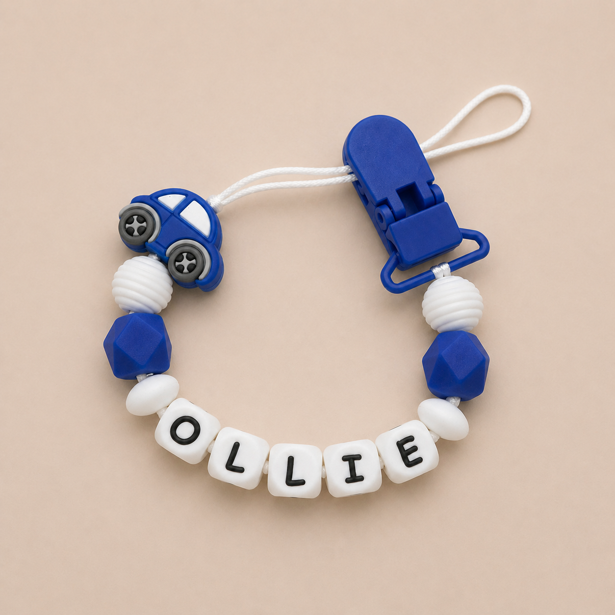 Silicone teether with blue car design and 'OLLIE' beads on a beige background