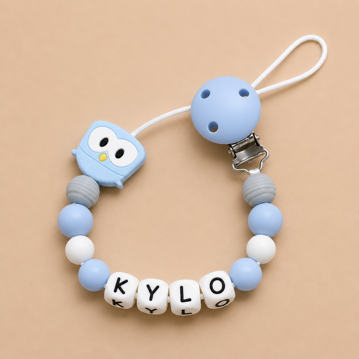 dummy clip with owl design and 'KYLO' beads on a beige background