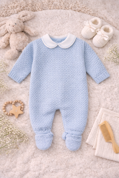 Peaceful newborn dressed in a baby blue Spanish-style knit outfit with classic collar, photographed in a soft, neutral setting.