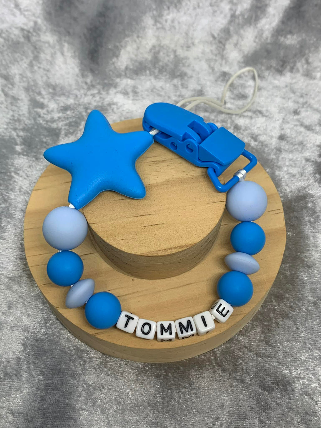 blue star Silicone pacifier Clip with blue star personalised with the name 'Tommie' on a grey textured surface. Can be personalised