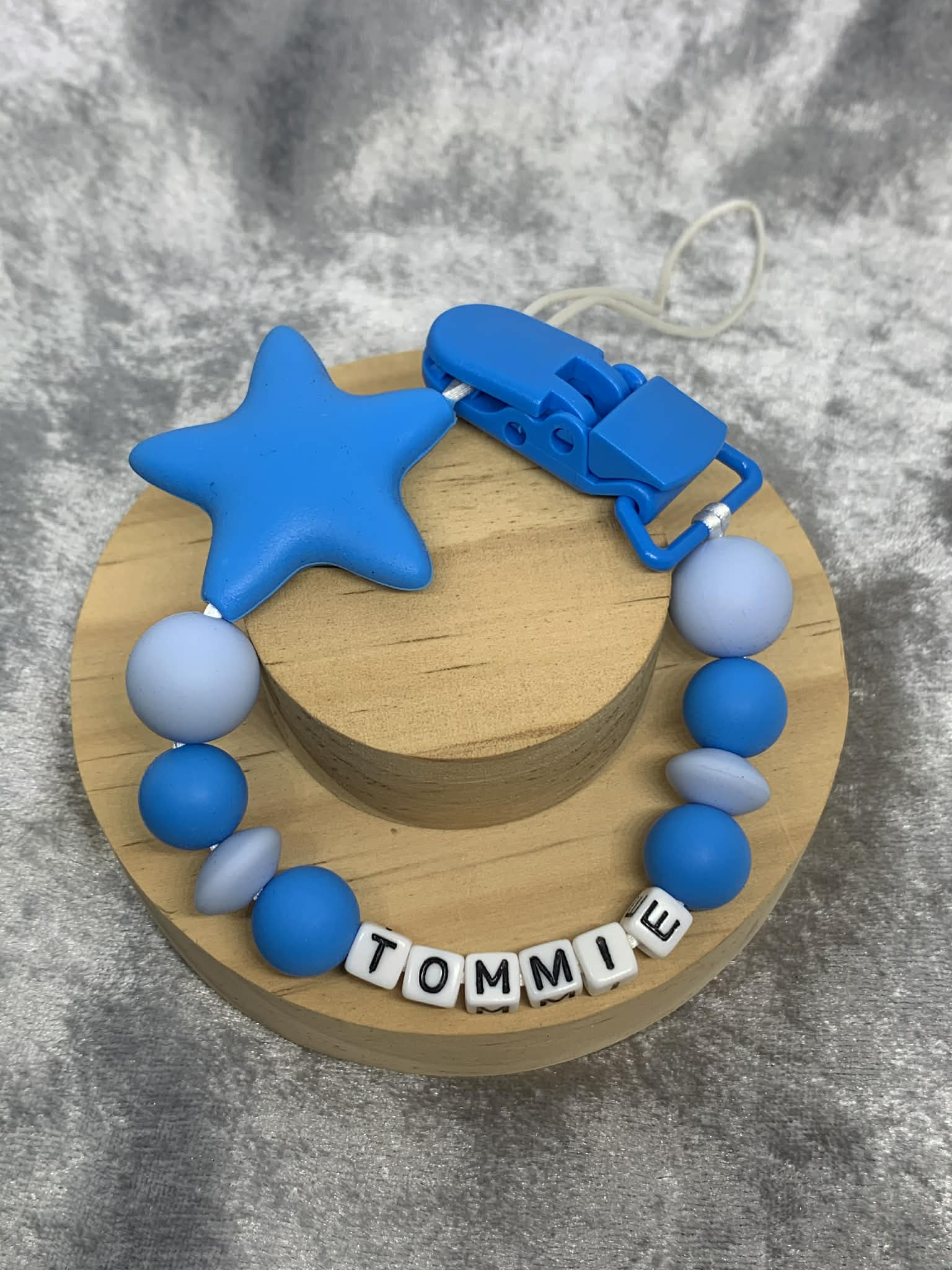 blue star Silicone pacifier Clip with blue star personalised with the name 'Tommie' on a grey textured surface. Can be personalised