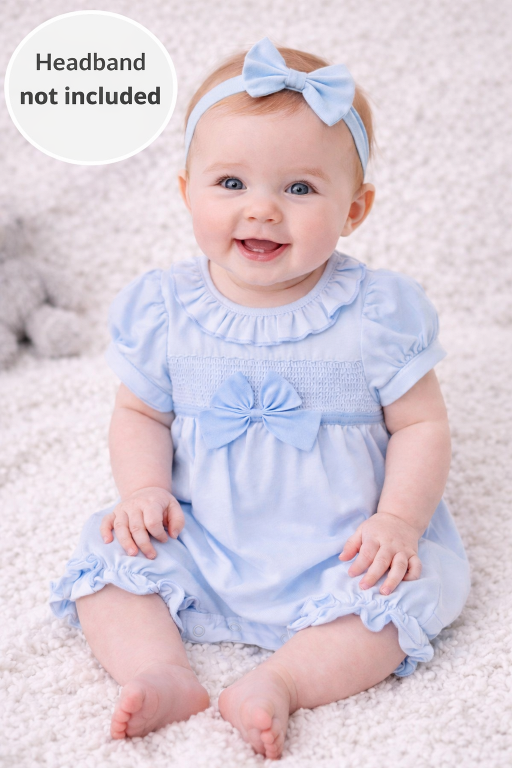 Baby wearing a light blue dress with ruffles and a bow on a white background