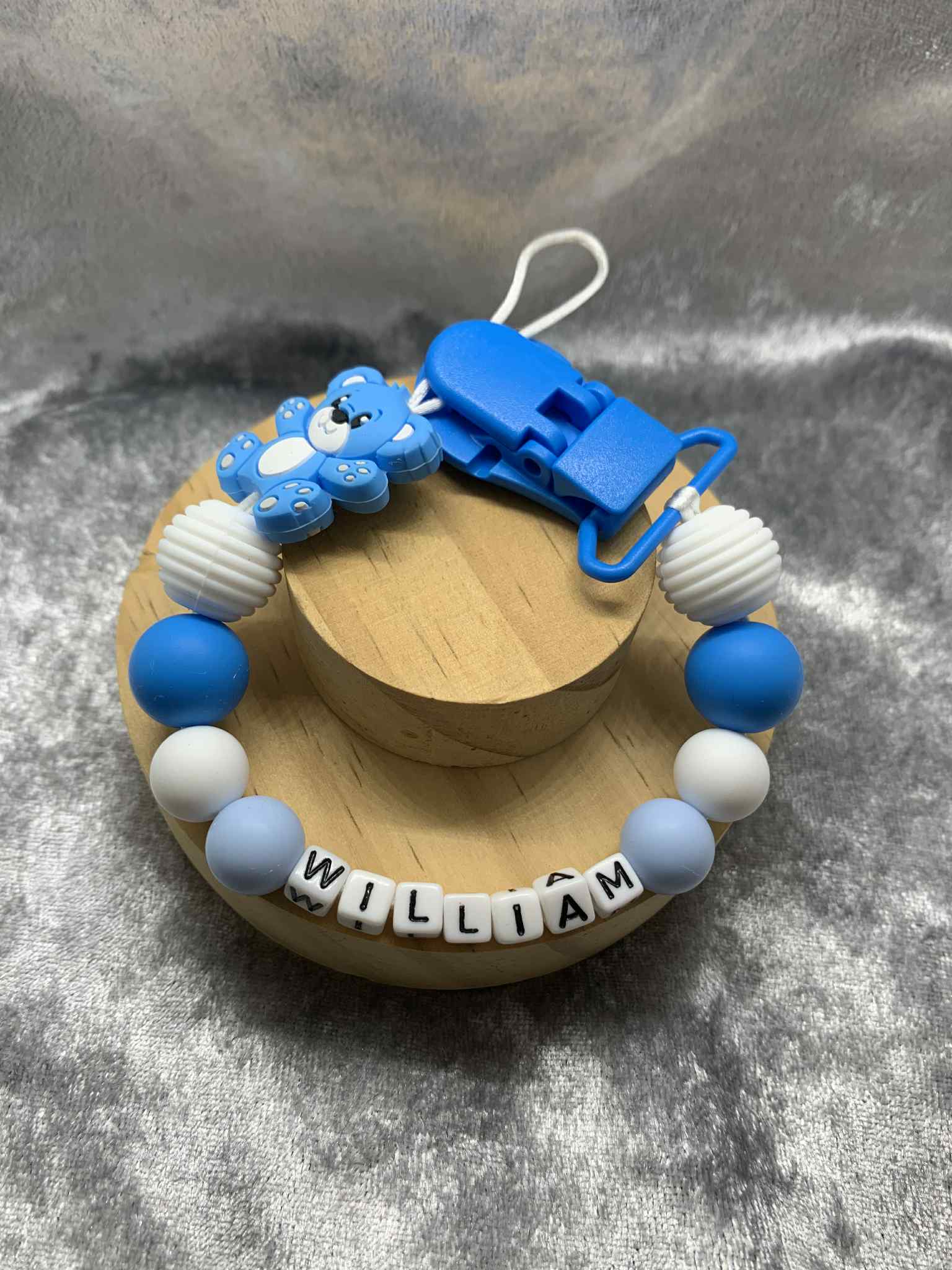 Blue and white teddybear dummy chain on a grey textured surface personalised with the name ''William'. Personalisation and MAM Adapter options available.