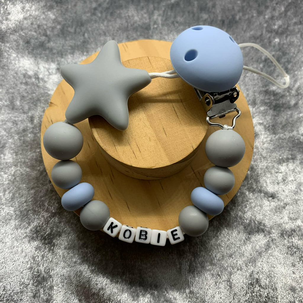 grey and blue Silicone Dummy Clip with greystar personalised with the name 'Kobie' on a grey textured surface. Can be personalised