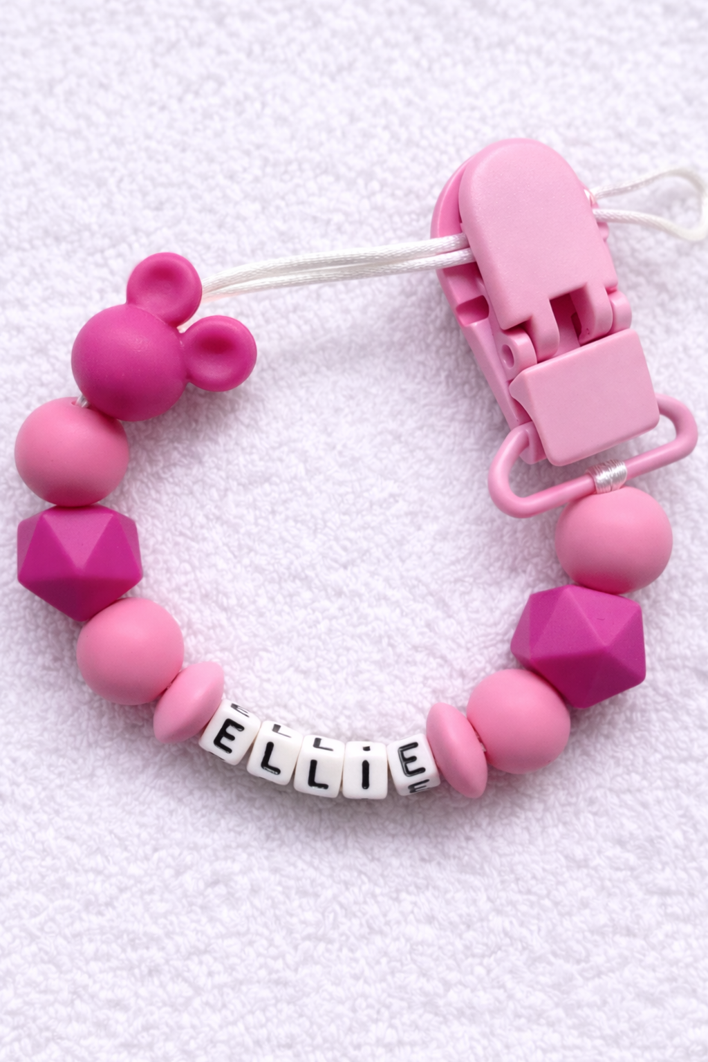 Pink baby dummy clip with 'ELLIE' name tag on a white background