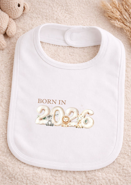 White bib with 'Born in 2026' text and decorative elements on a soft surface.