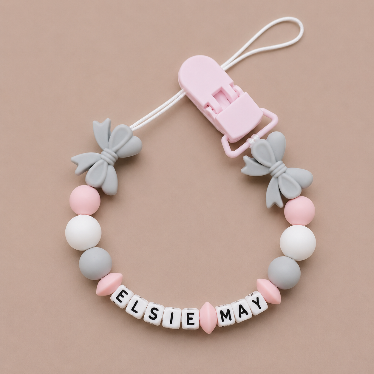 Baby dummy clip with colorful beads and 'Elsie May' name on a beige background