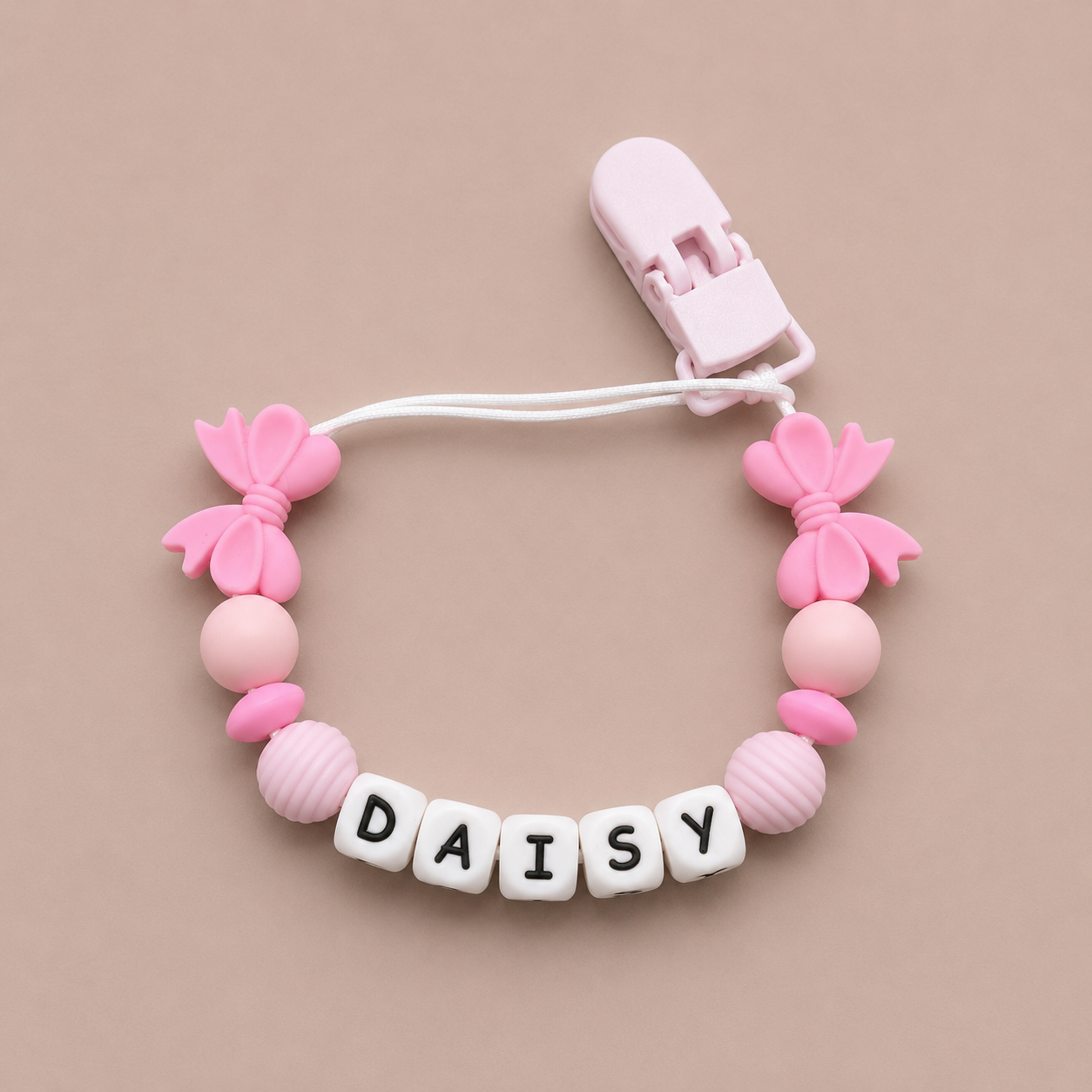 Pink baby dummy clip with 'DAISY' beads on a beige background