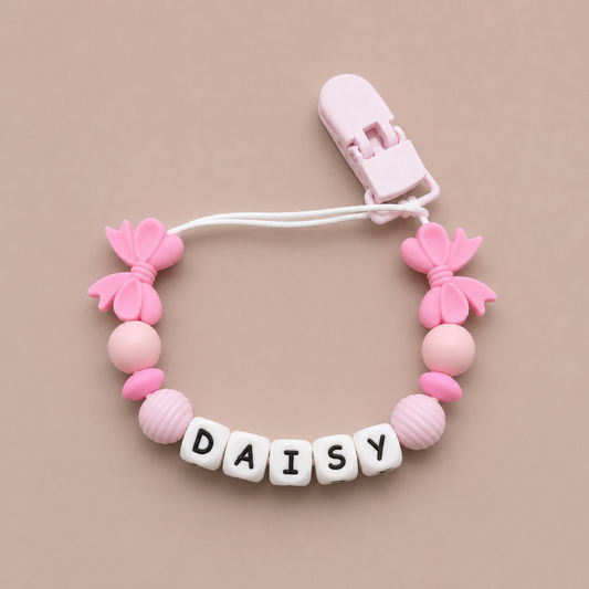 Pink baby dummy clip with 'DAISY' beads on a beige background