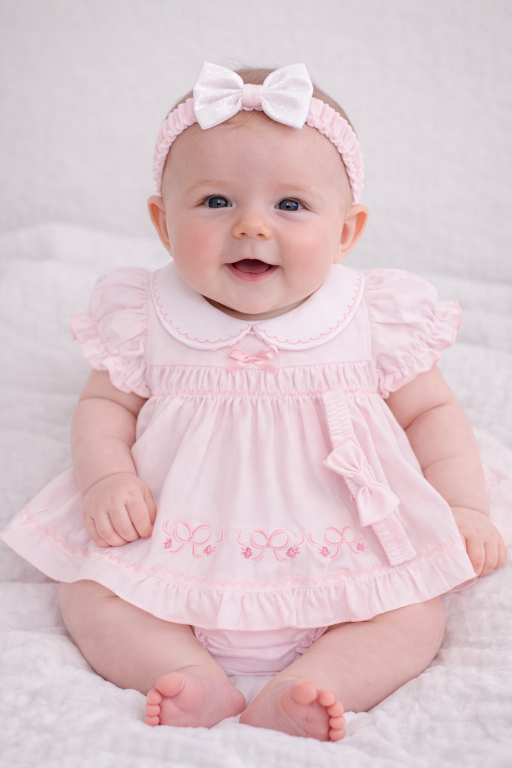 Baby wearing a pink dress with ruffles and a matching headband on a white background