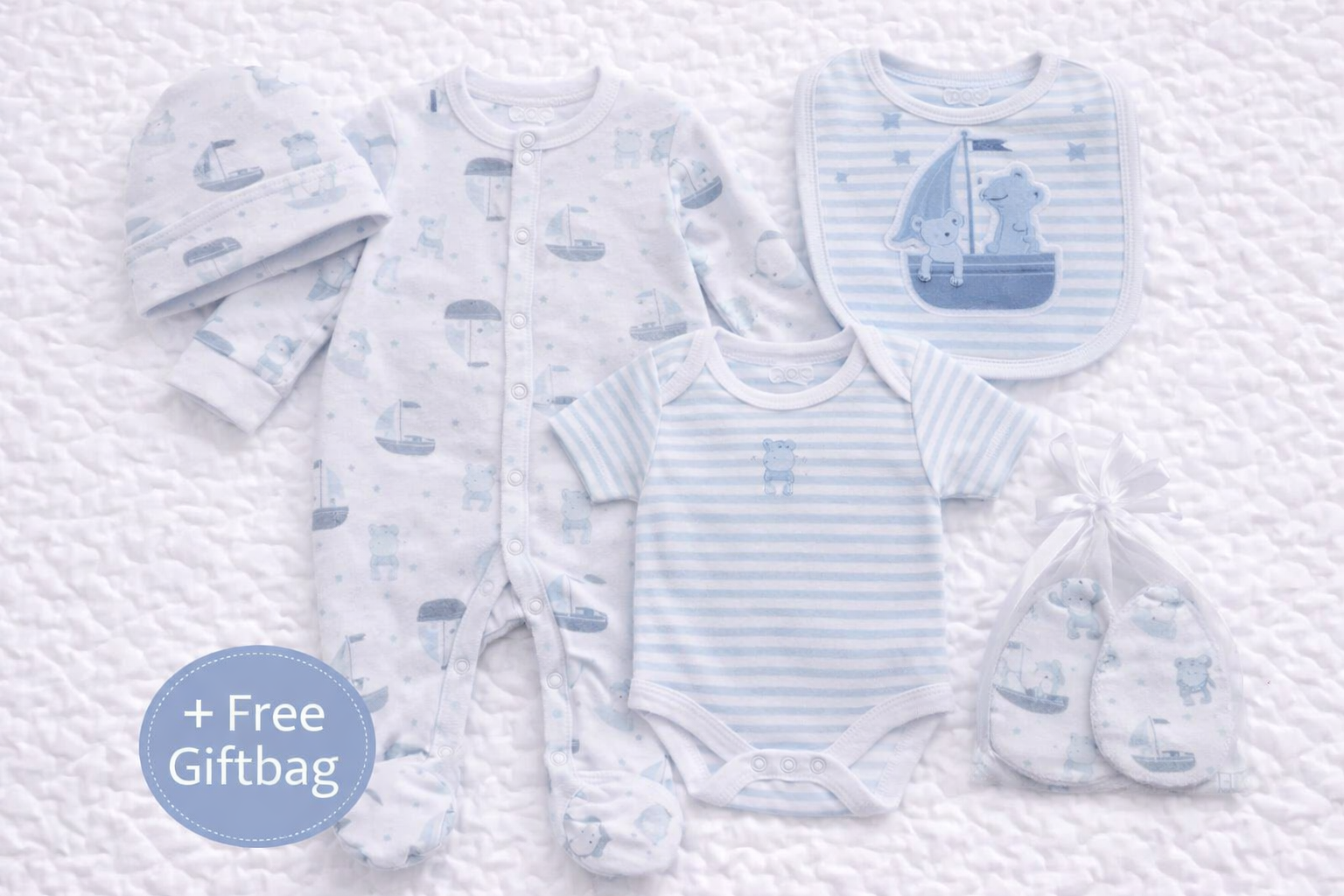 A coordinated baby boys 5-piece clothing set laid out on a white quilted background, featuring a light blue animal-print babygrow with all-white sleeves, a matching long-sleeved striped bodysuit, coordinating bib with bear and sailboat design, printed baby hat, and matching scratch mittens presented in a sheer gift bag. A blue circle highlights “+ Free Giftbag,” making the set gift-ready and ideal for newborns or baby showers.