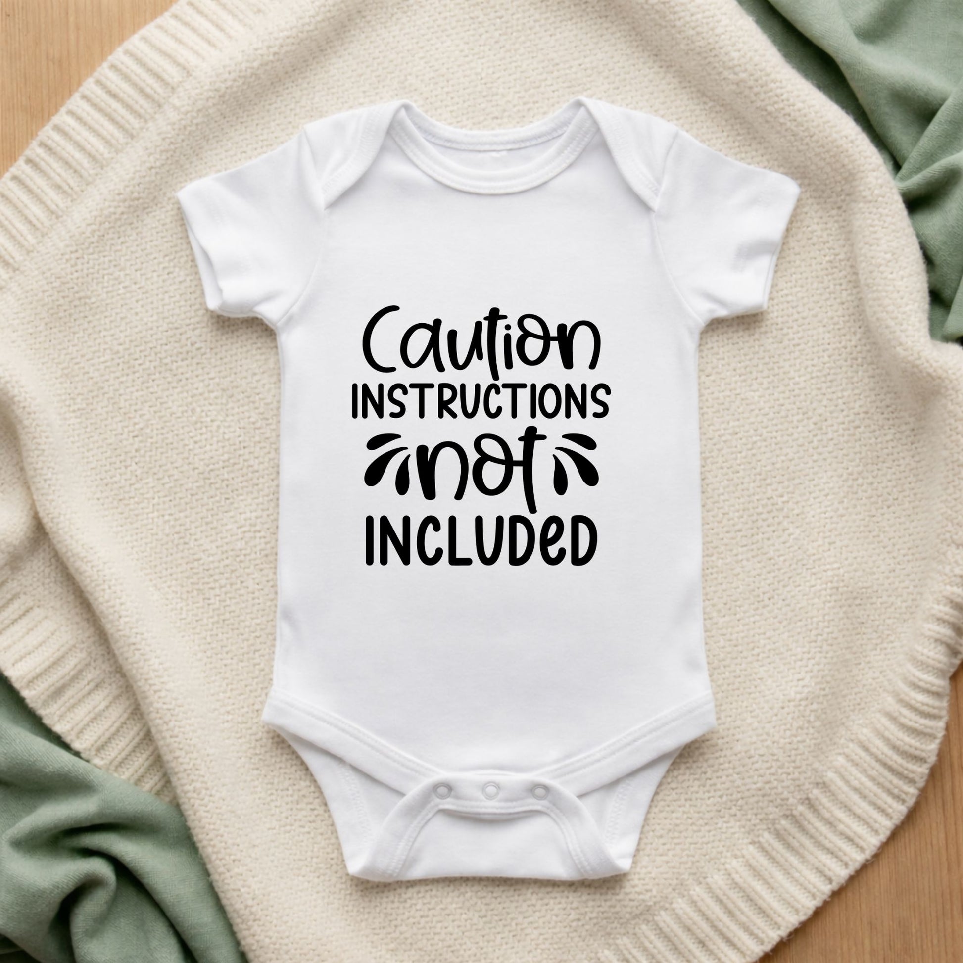 White baby onesie with 'Caution Instructions Not Included' text on a textured surface.