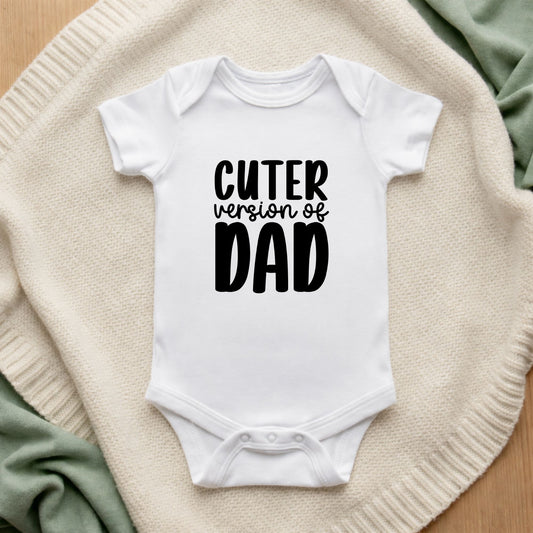 White baby onesie with 'Cuter version of Dad' text on a textured surface