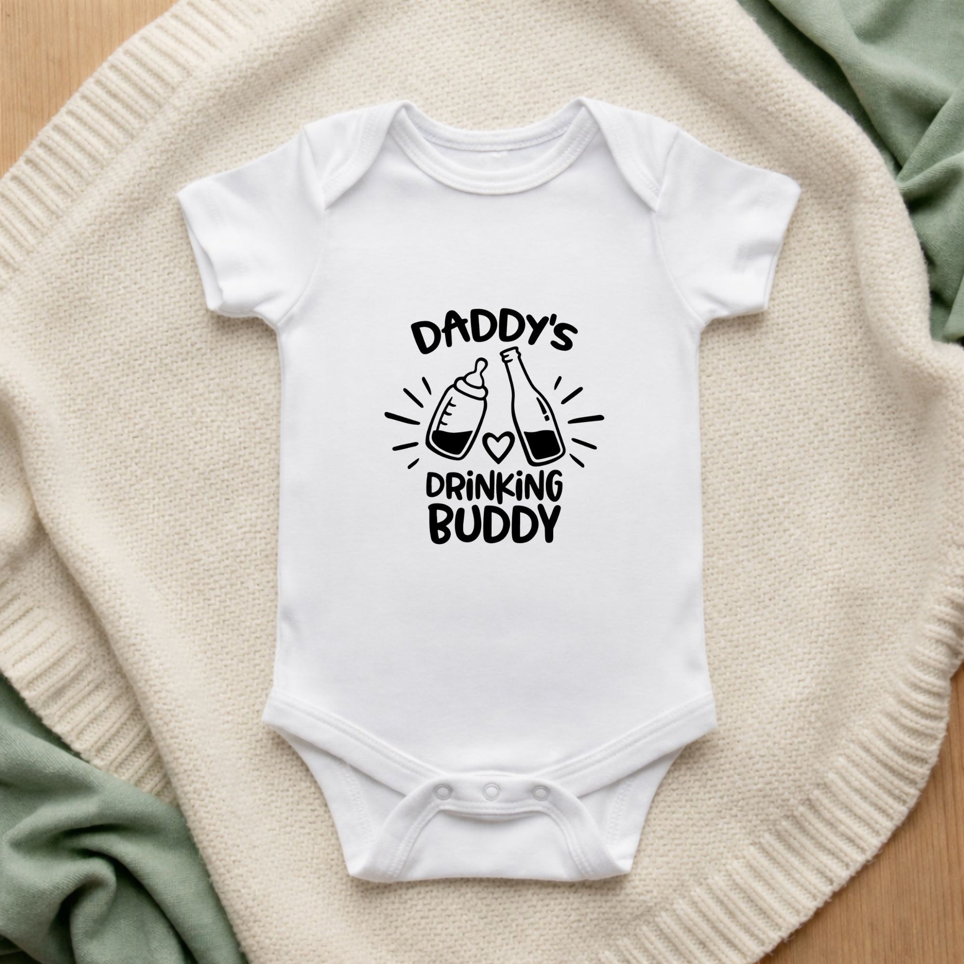 White baby onesie with 'Daddy's Drinking Buddy' text on a textured surface