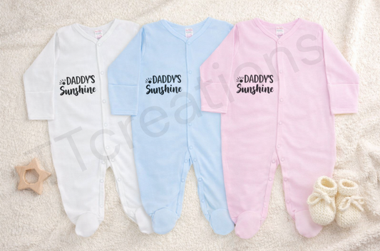 white, blue, and pink baby sleepsuits with the text “Daddy’s Sunshine” displayed on a neutral background.