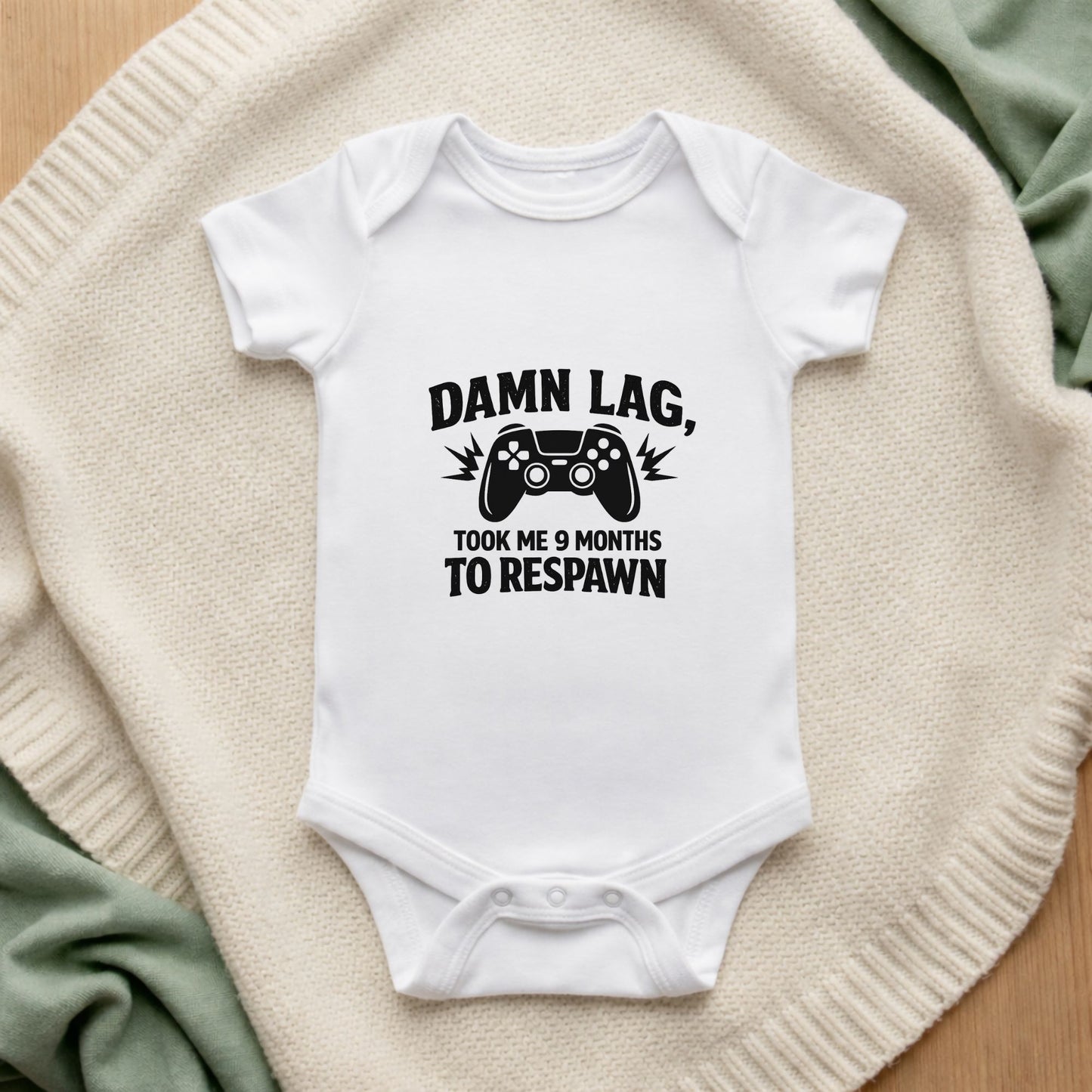 White baby onesie with text and gaming controller graphic on a textured surface