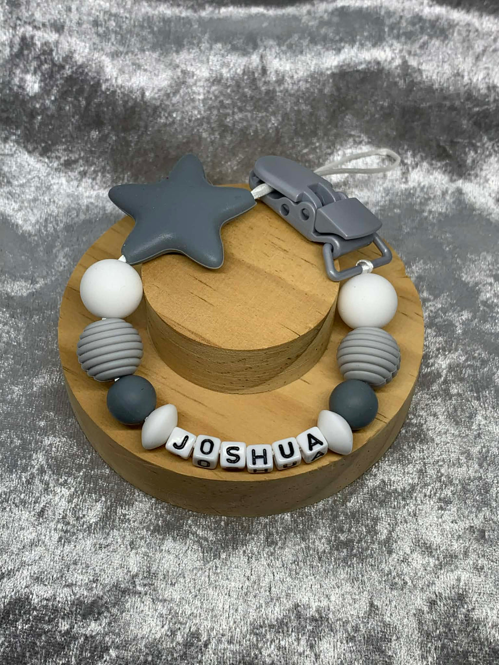 Dark Grey & White Silicone Dummy Clip with Dark Grey star personalised with the name 'Joshua' on a grey textured surface. Can be personalised