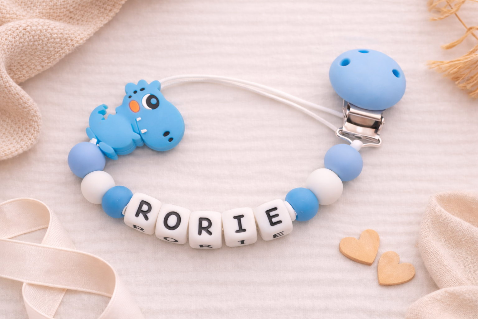Flat lay of a personalised blue dinosaur dummy clip with custom name