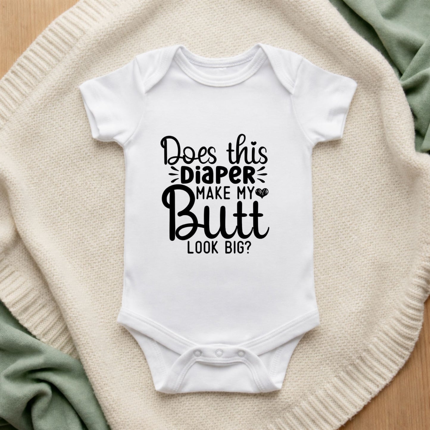 White baby onesie with humorous text on a textured surface Does This Diaper Make My Butt Look Big Baby Bodysuit