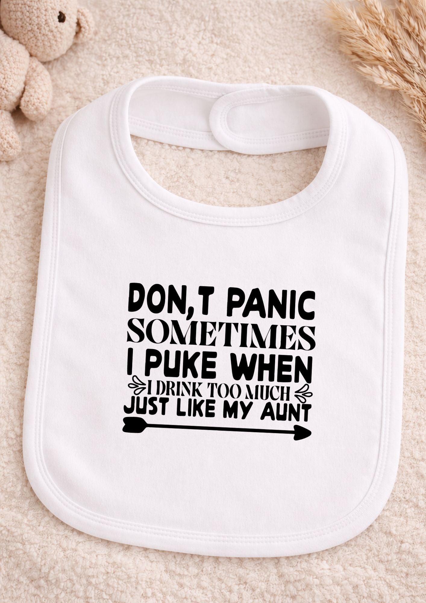 White baby bib with humorous text on a beige surface Don't Panic Sometimes I Puke Just Like My Aunt Baby Bib | Funny Newborn Gift