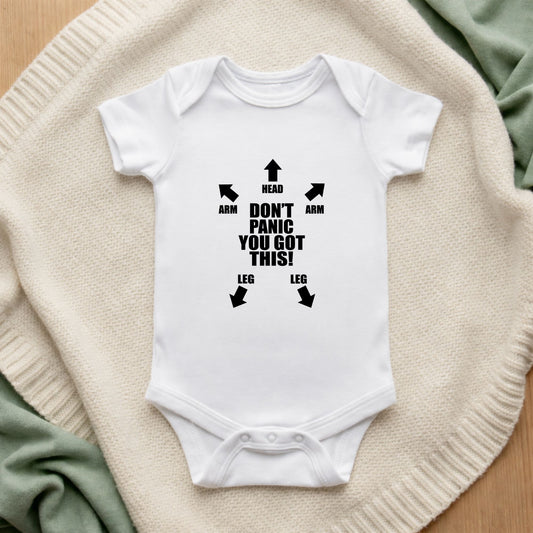 White baby onesie with black text and arrows on a beige surface