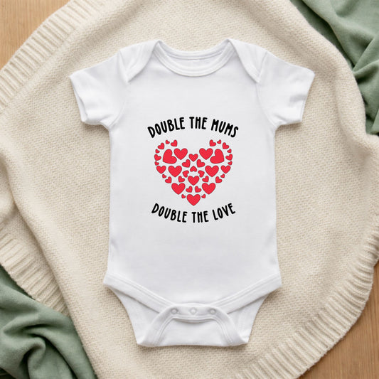 White baby onesie with heart design and text on a textured surface Double The Mums Double The Love Baby Bodysuit