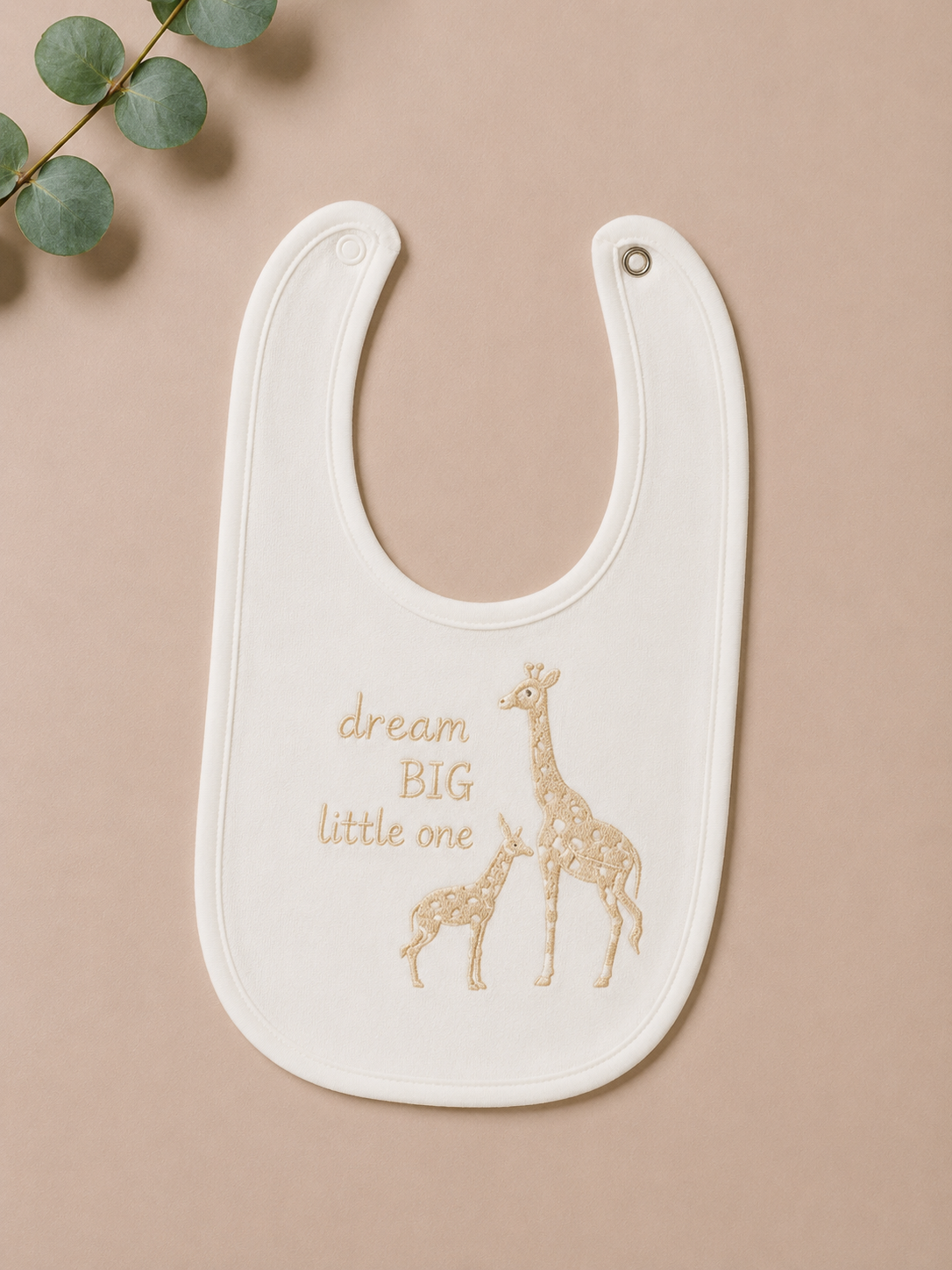 White bib with gold text and giraffe design on a beige background